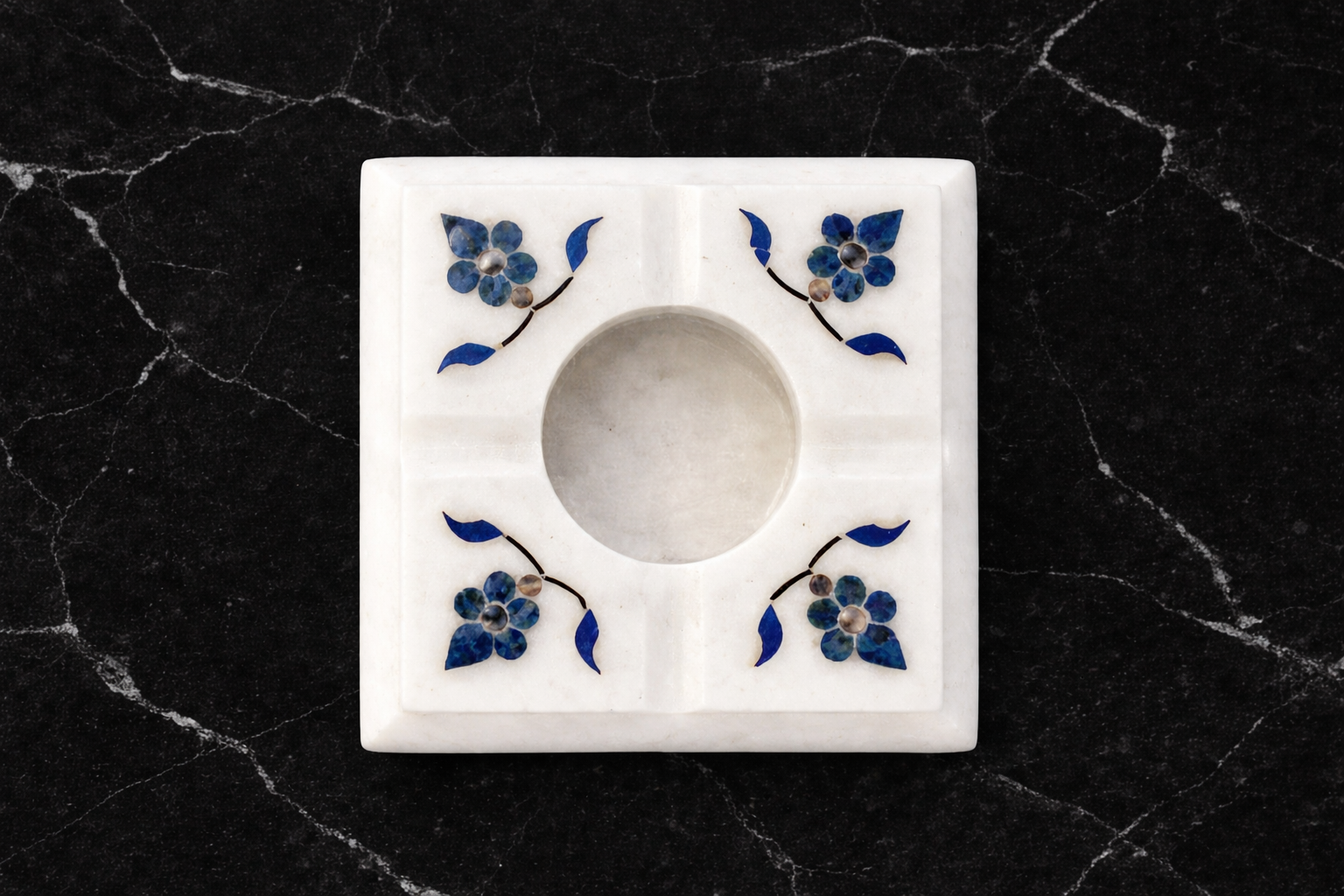 White marble ashtray with blue floral inlay design on black marble table