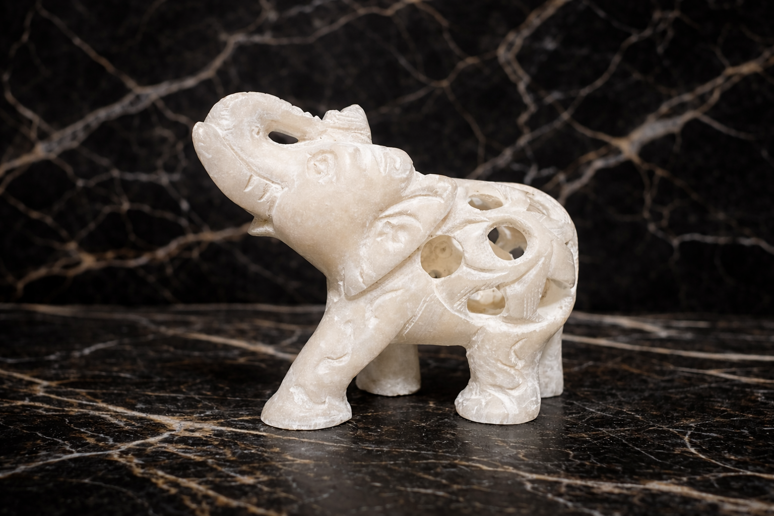 Side view of hand carved white marble elephant sculpture elephant within elephant design on black marble surface