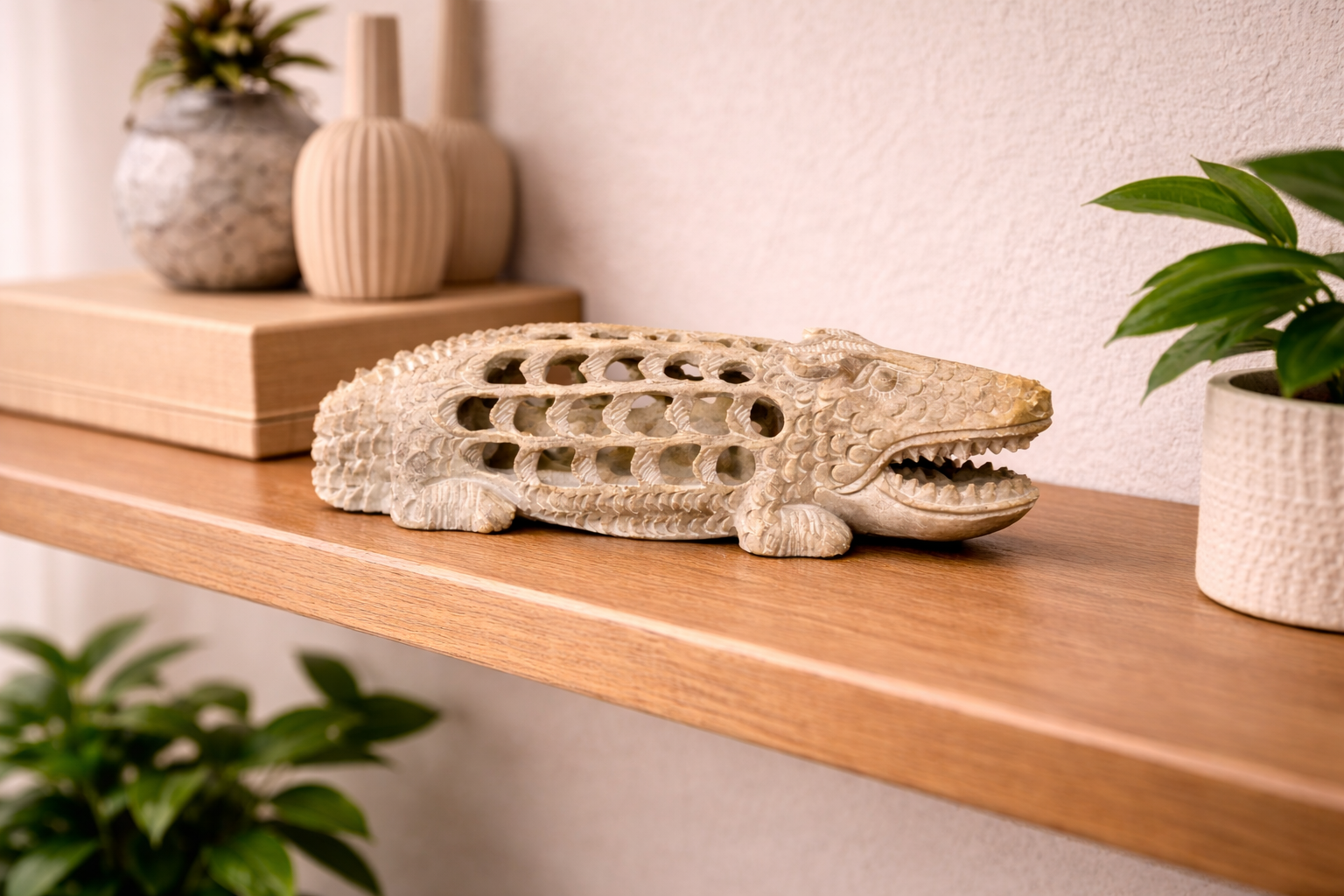 Hand-carved soapstone crocodile figurine with hollow carving displayed on wooden shelf with indoor plants and vases