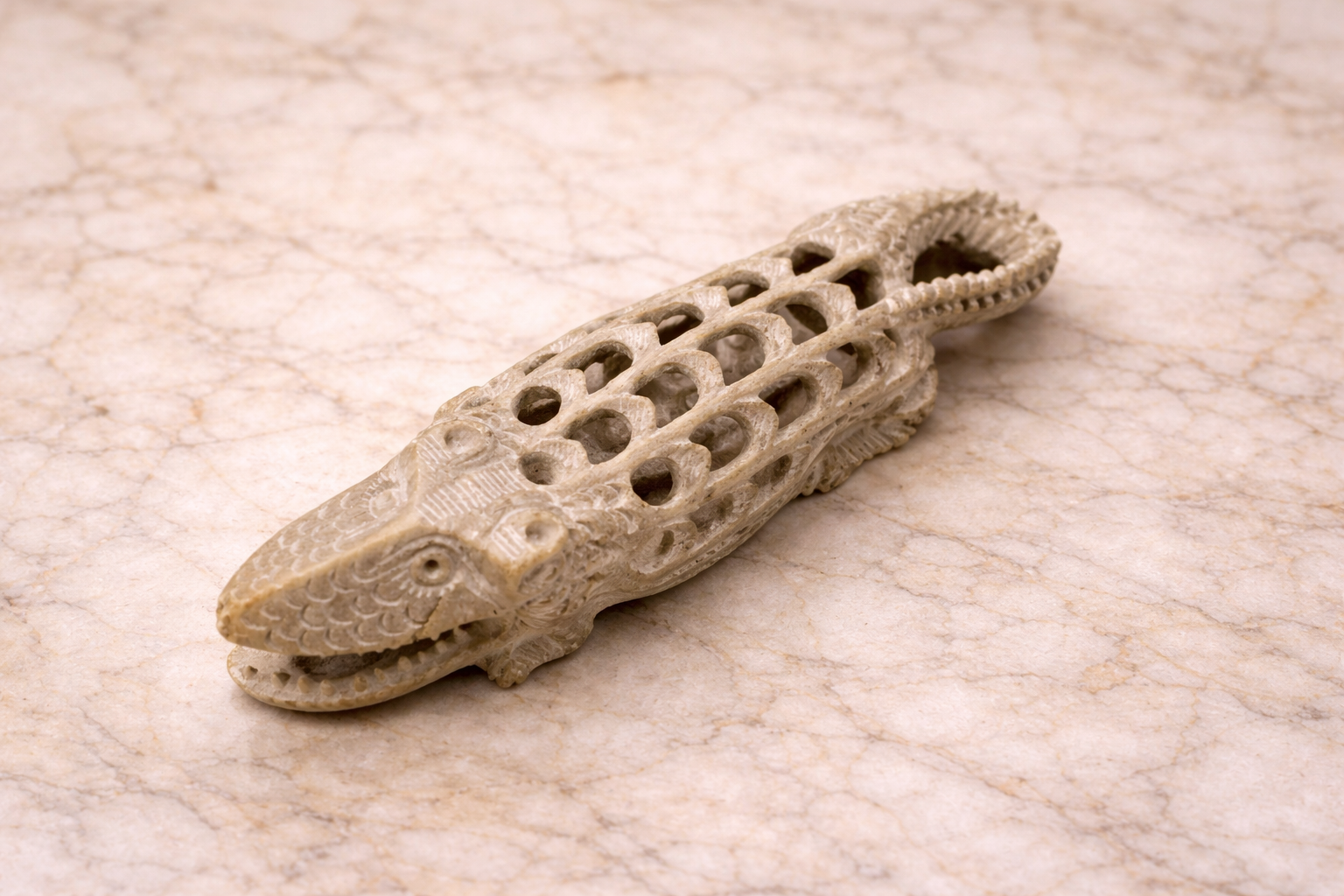 Hand-carved soapstone crocodile figurine with intricate hollow lattice carving on marble surface