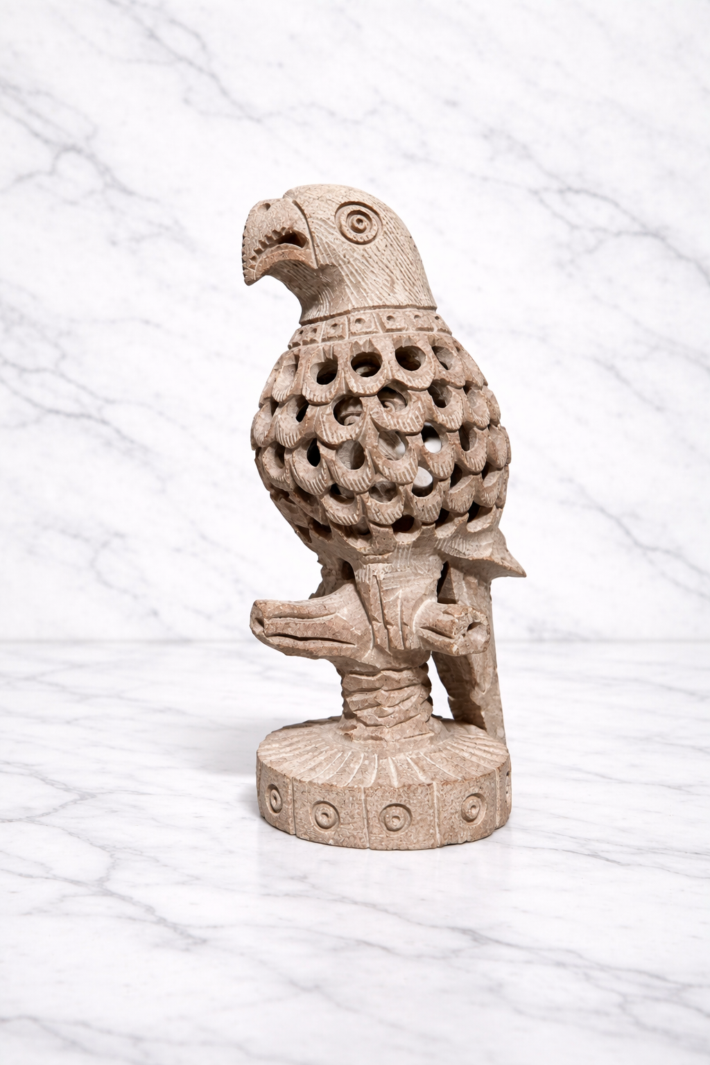 Hand-carved soapstone parrot sculpture with detailed openwork feather carving on marble background