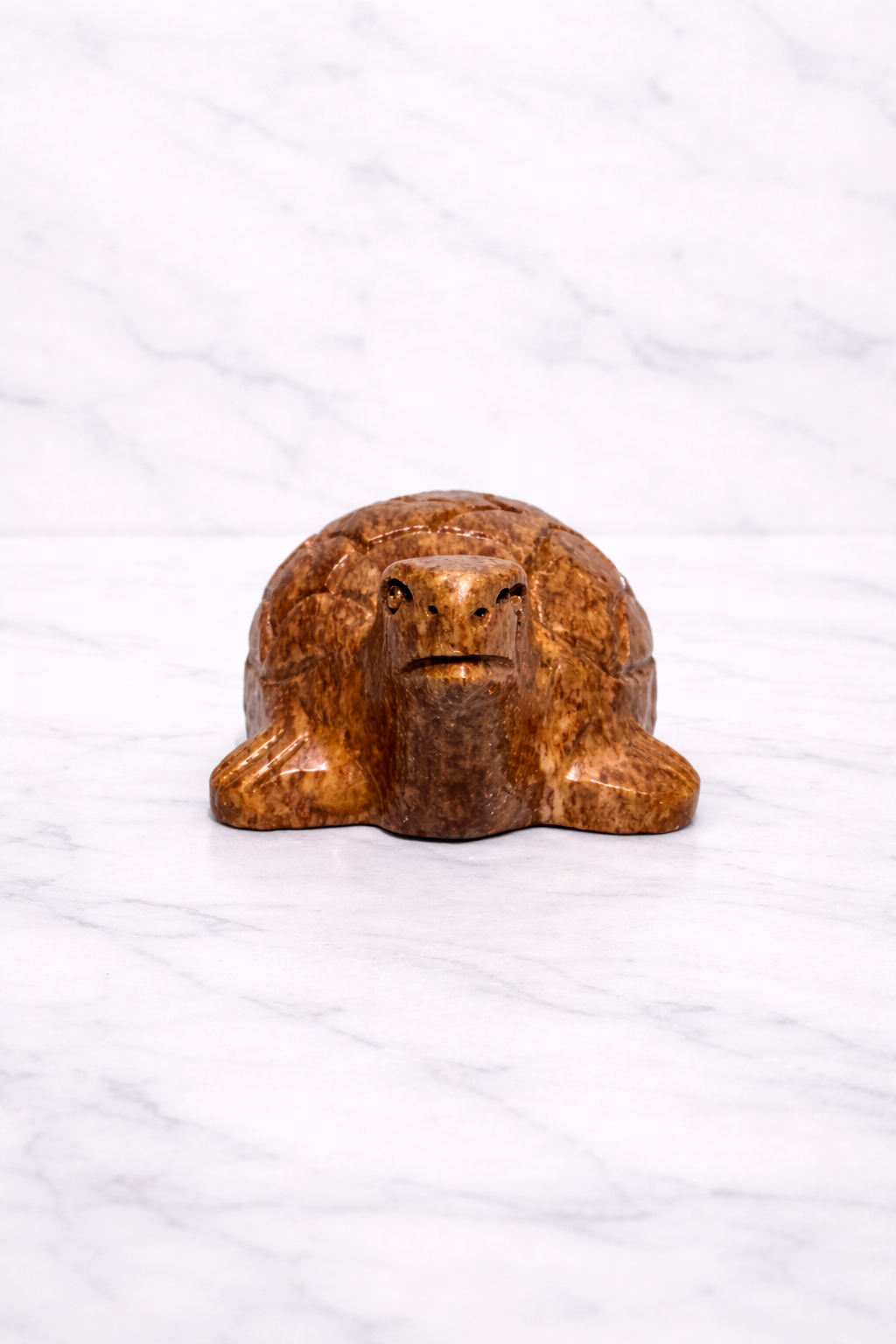 Front view of Hand-carved polished soapstone turtle sculpture on white marble surface