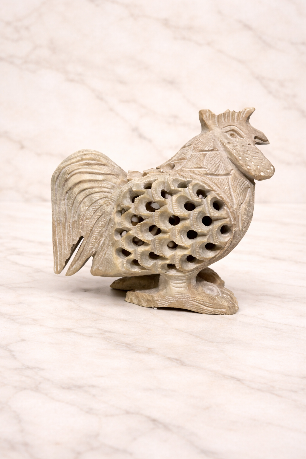 Soapstone rooster sculpture with openwork carving displayed on marble background