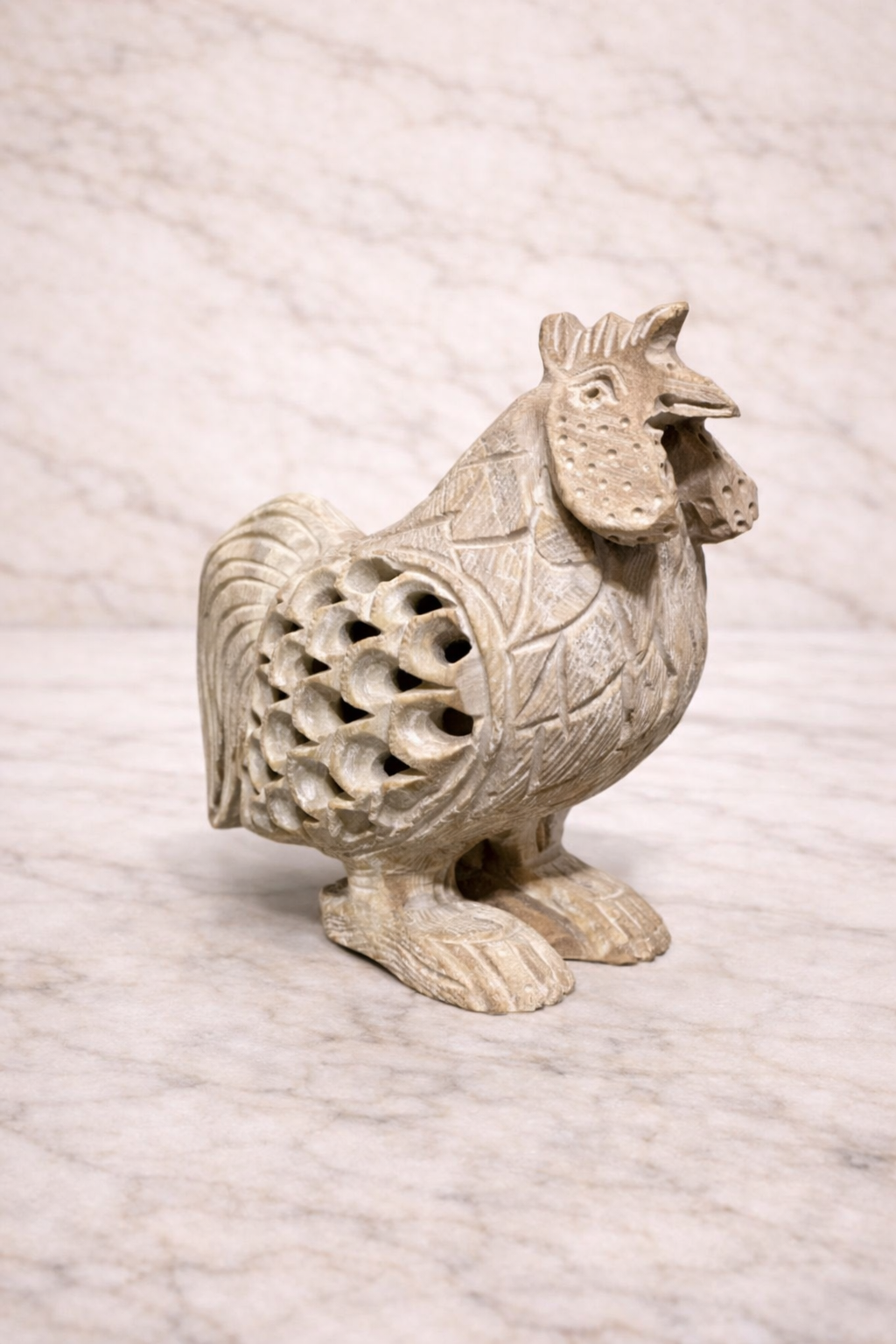 Hand-carved soapstone rooster sculpture with openwork jali carving on light marble background