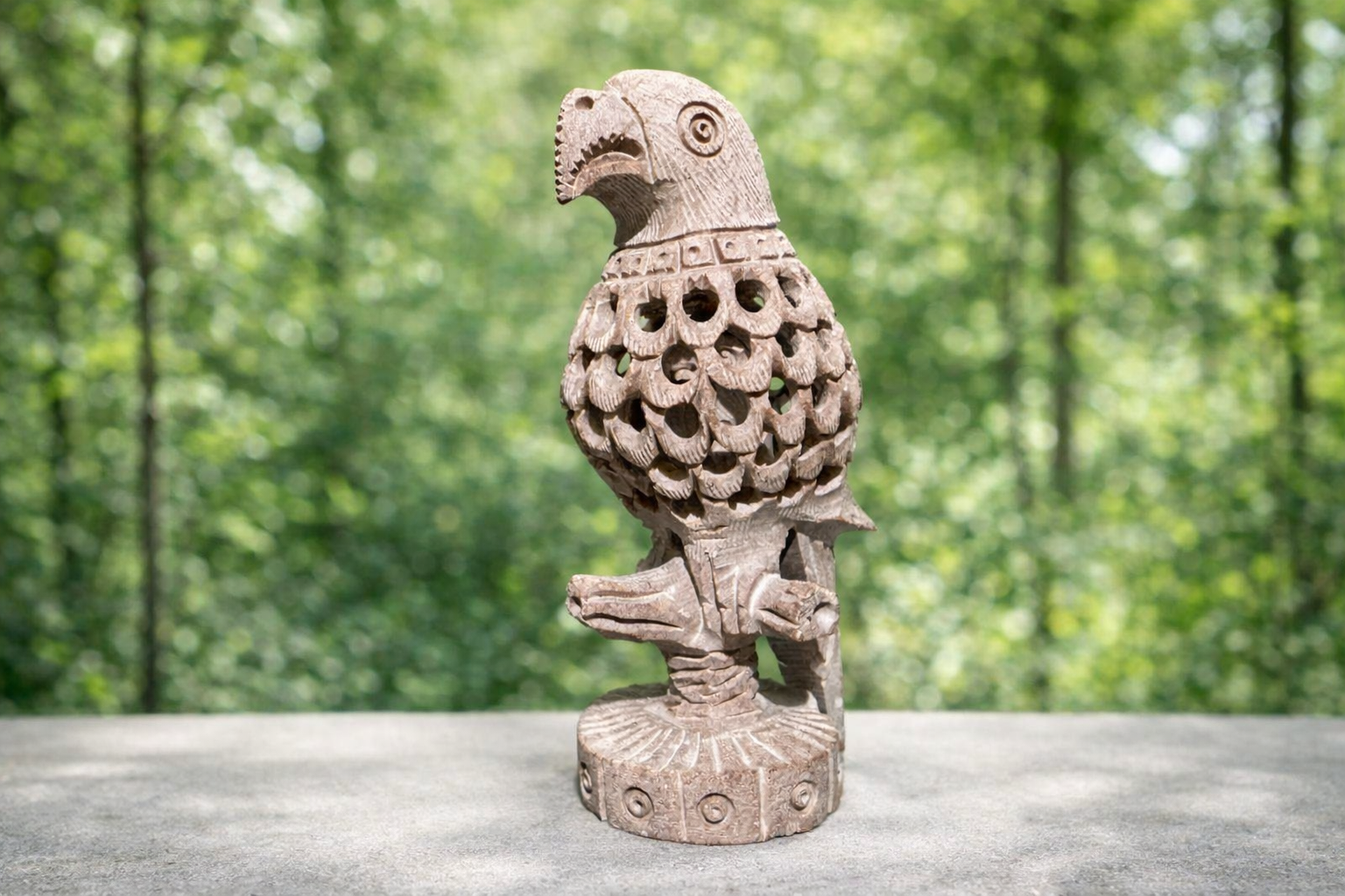 Hand-carved soapstone parrot sculpture with openwork feather detailing displayed against natural green background