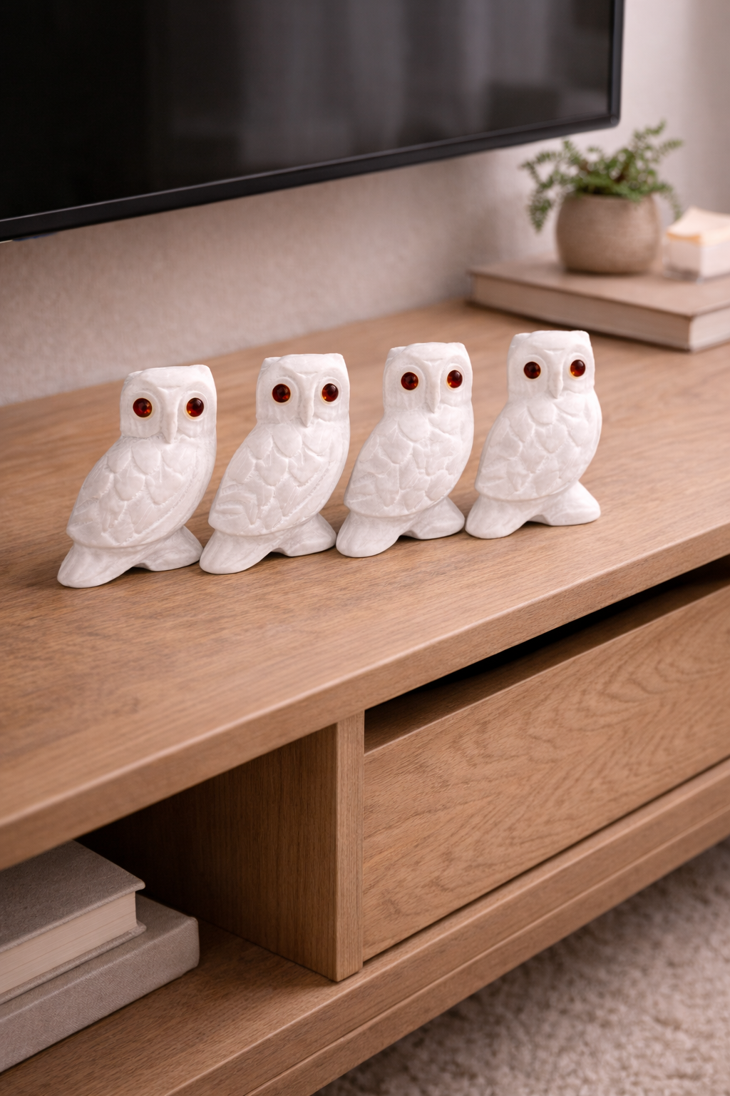 Four white marble owl figurines with red stone eyes styled on wooden console table in modern living room