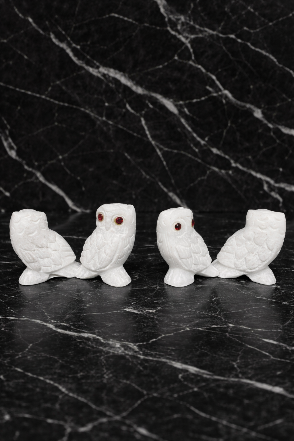 Set of four hand-carved white marble owl figurines with polished finish on black marble background