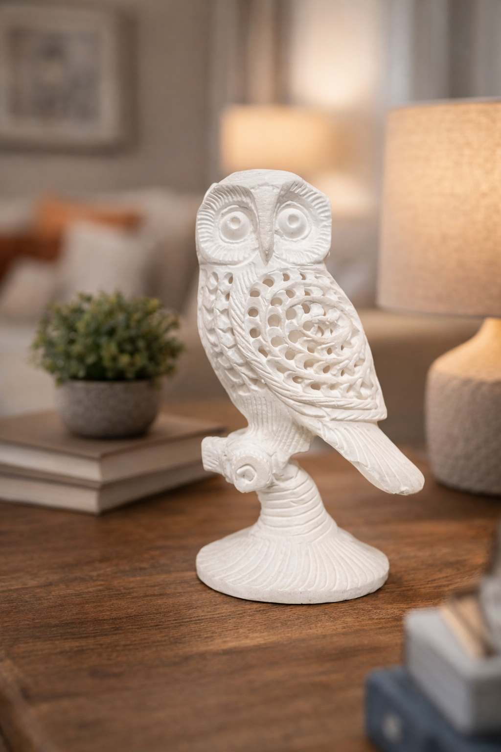 Hand-carved white marble owl sculpture on wooden table with lamp and books in living room setting