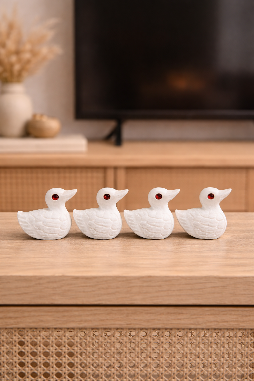 Four hand-carved white marble duck figurines with red stone eyes displayed on a wooden console table in a modern home setting, luxury stone décor NZ.