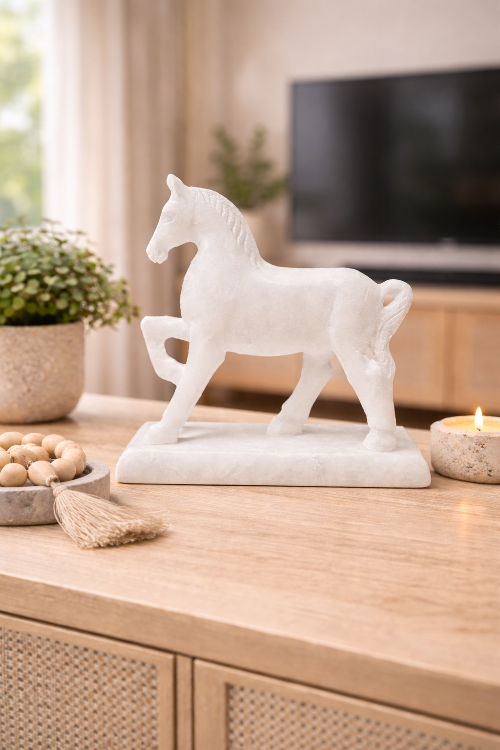 White marble horse sculpture on stand styled on wooden console table with candle and living room background