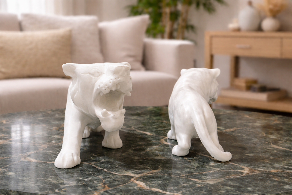 Two white marble tiger sculptures displayed on a green marble table in a modern living room setting.