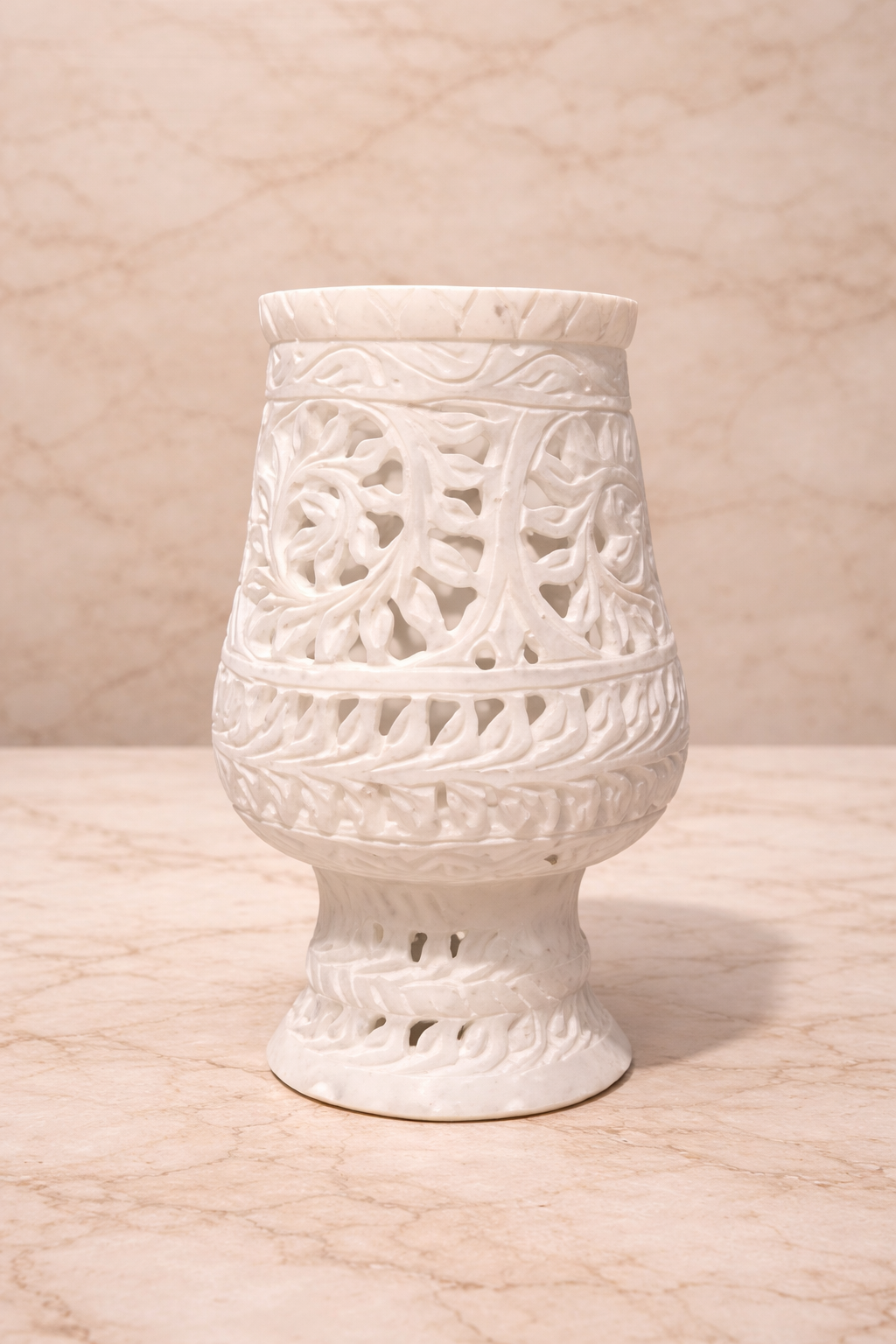 Hand-carved white marble lantern-style candle holder with intricate floral cutwork on neutral stone surface