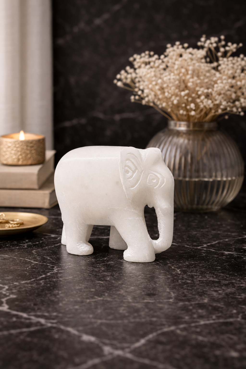 Polished white marble elephant sculpture on black marble table with warm lamp and flowers in background