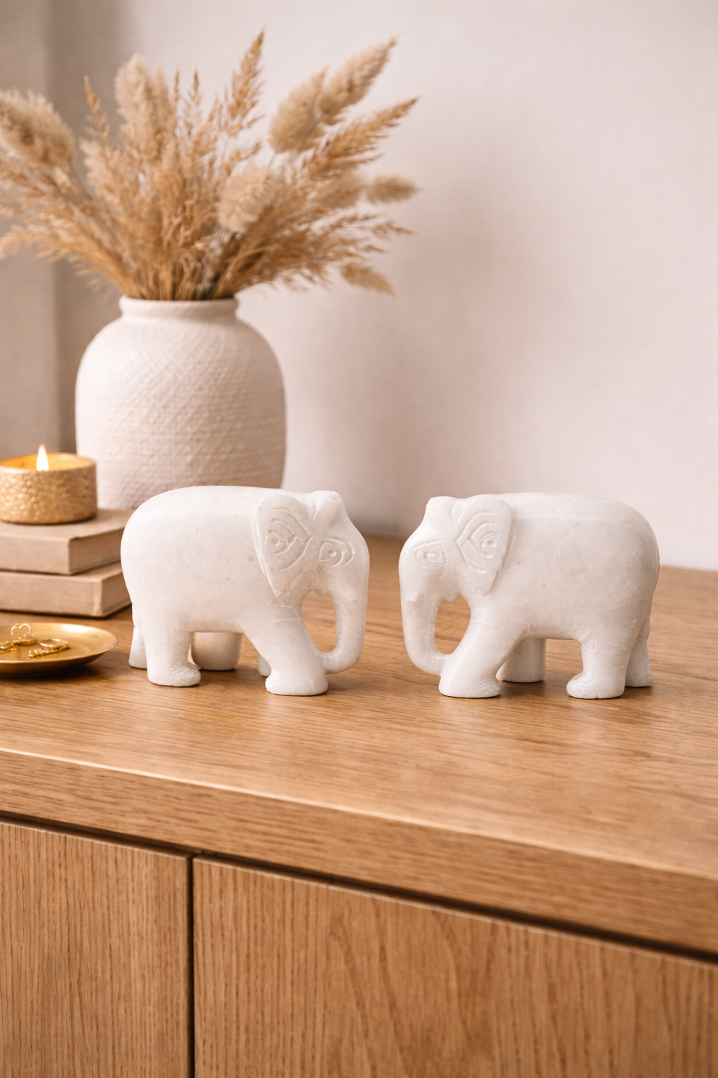 Pair of polished white marble elephant sculptures on wooden table with candle and décor