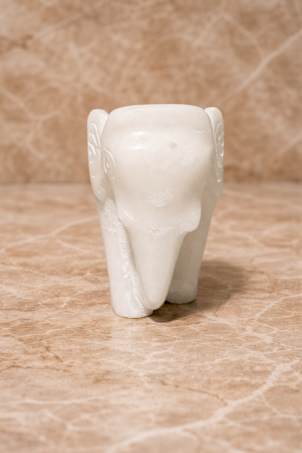 Front view of polished white marble elephant sculpture on beige marble surface
