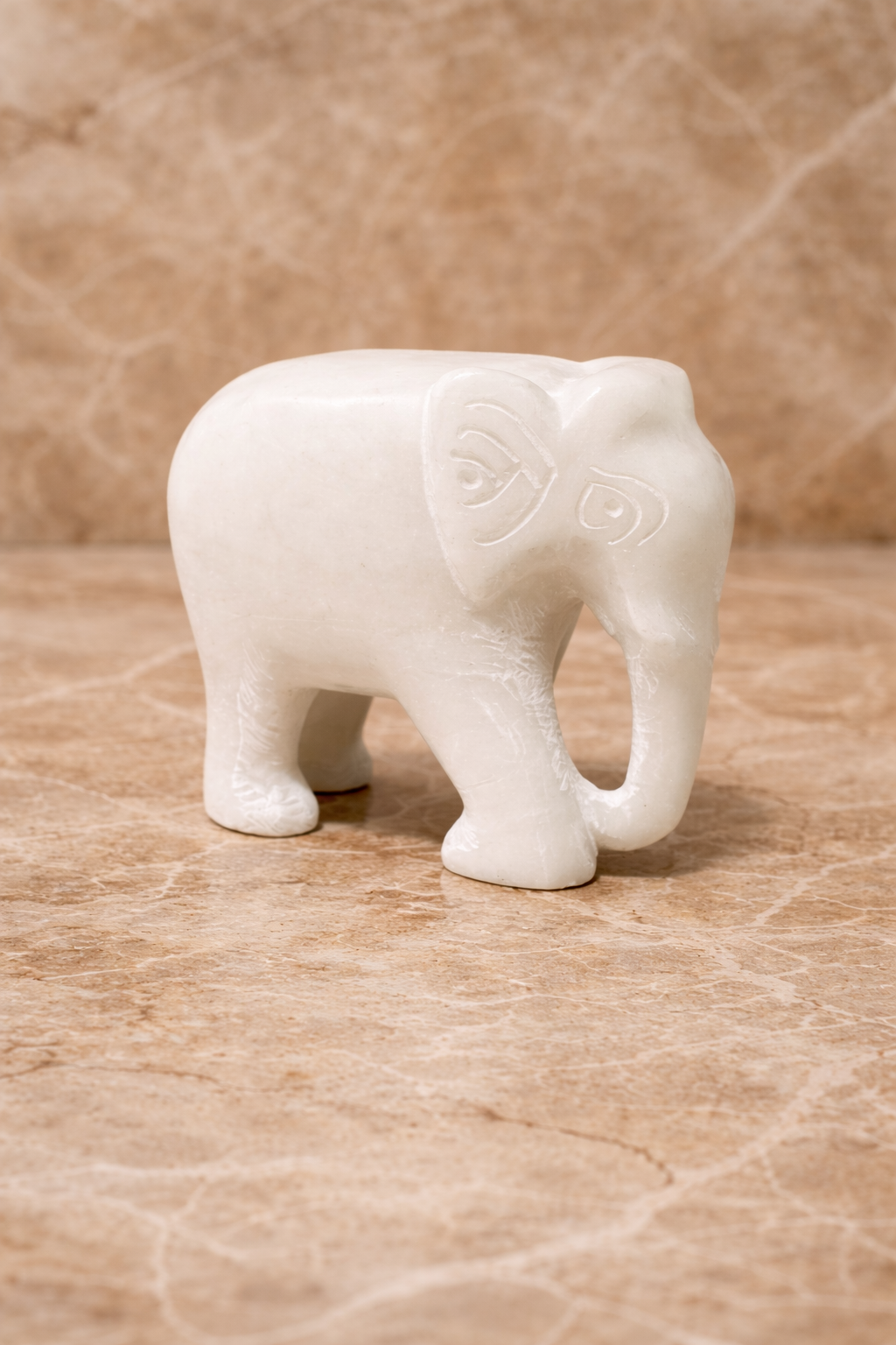 Side view of polished white marble elephant sculpture on beige marble surface