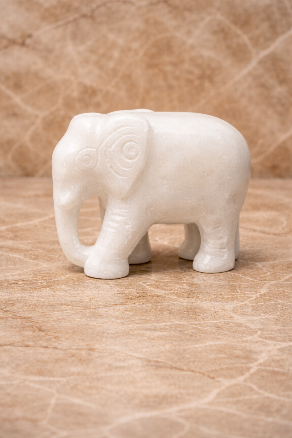 Side view of polished white marble elephant sculpture on beige marble surface