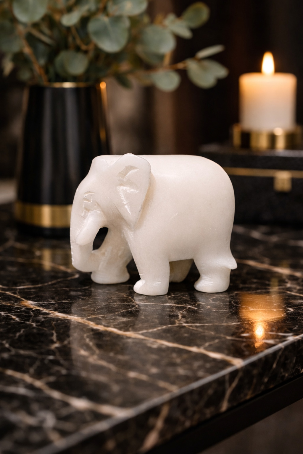 0.272 kg Polished white marble elephant sculpture on black marble table with candle and plant in background