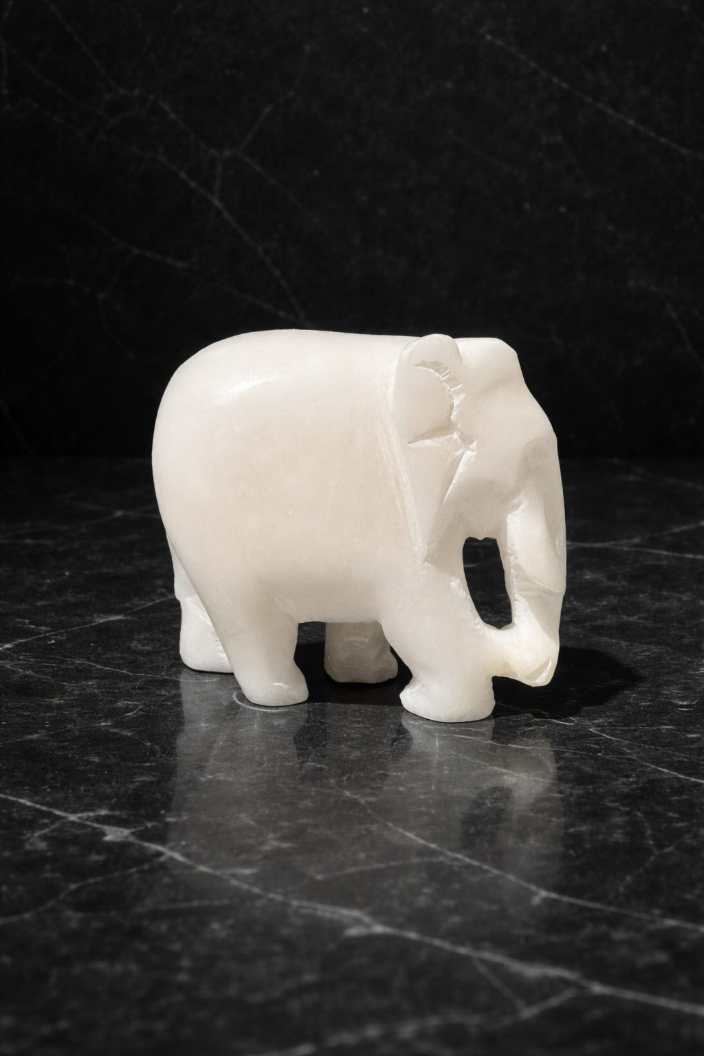 Polished white marble elephant sculpture on black marble table with candle and plant in background