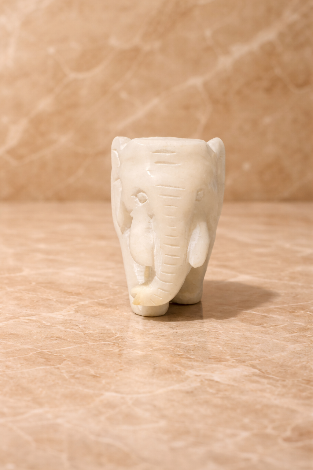 Front view of polished white marble elephant sculpture on beige marble surface