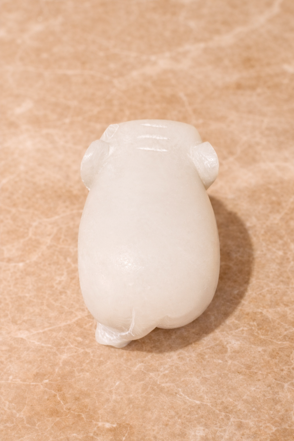 Top view of polished white marble elephant sculpture on beige marble surface