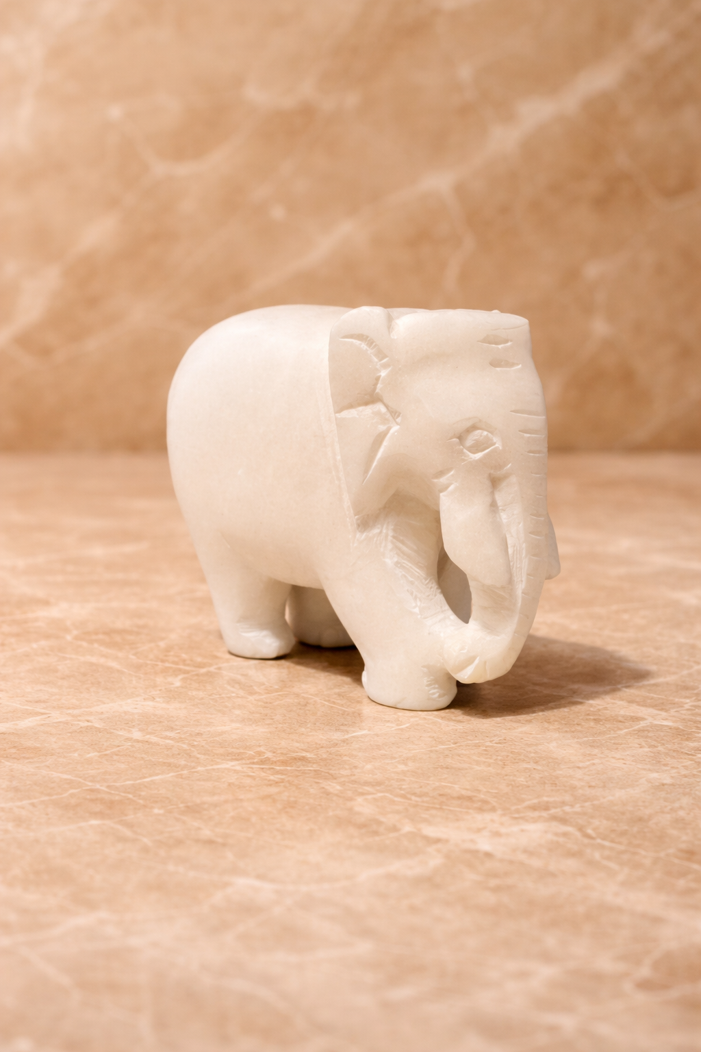 Side view of polished white marble elephant sculpture on beige marble surface