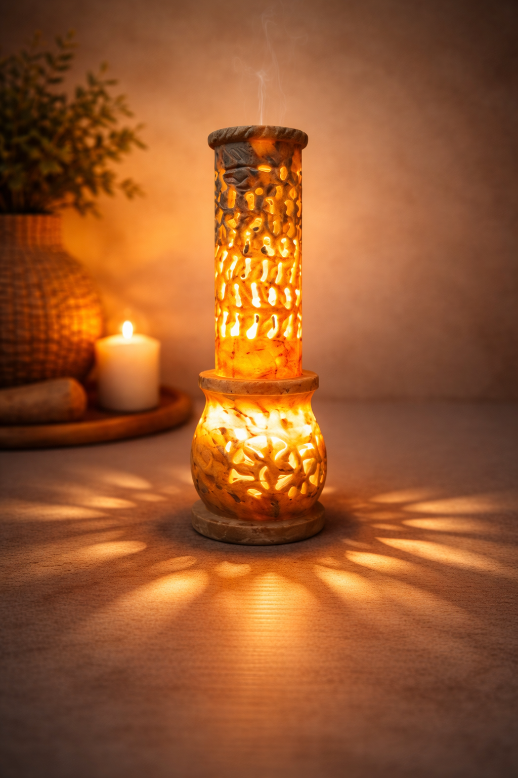 Hand-carved soapstone incense burner tower glowing on wooden table with candle and plant in background