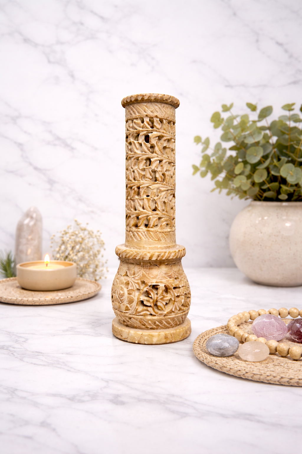 Hand-carved soapstone incense burner tower on white marble surface with candle, crystals and indoor plant