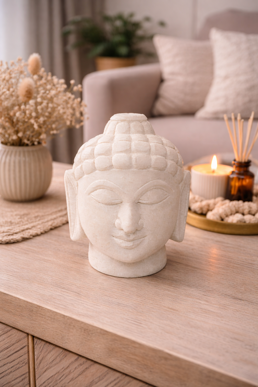 White marble Buddha head statue styled on living room table with candle and vase decor