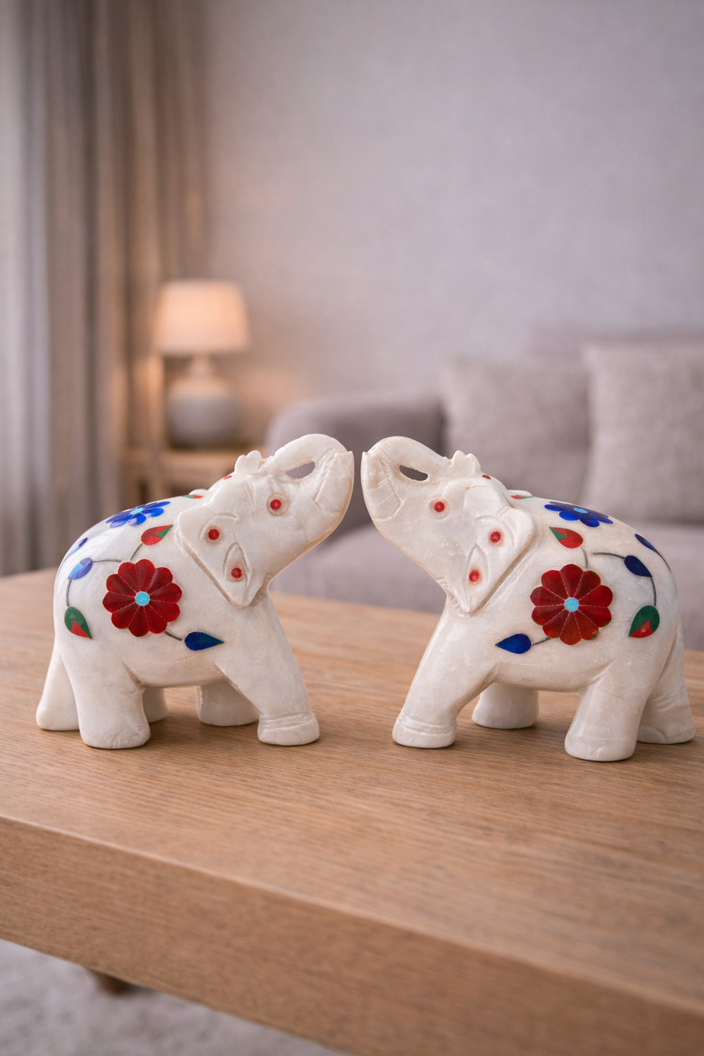 Pair of hand-carved white marble elephant figurines with colourful floral inlay facing each other on a wooden table.