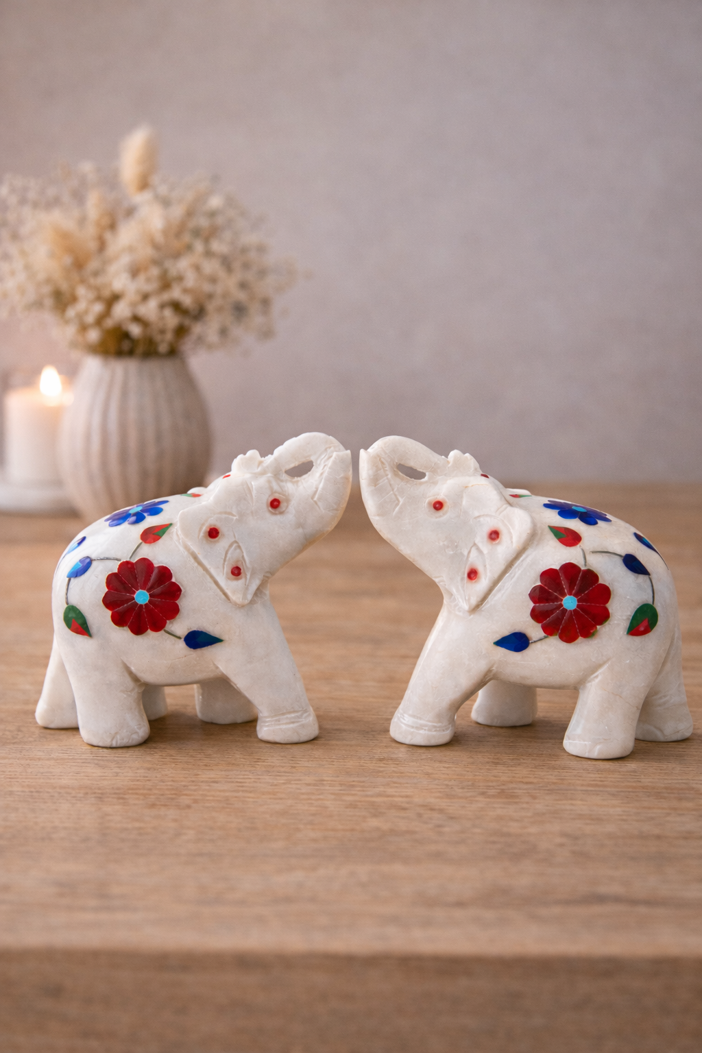 Two decorative white marble elephant sculptures with colourful stone inlay displayed on a wooden table.