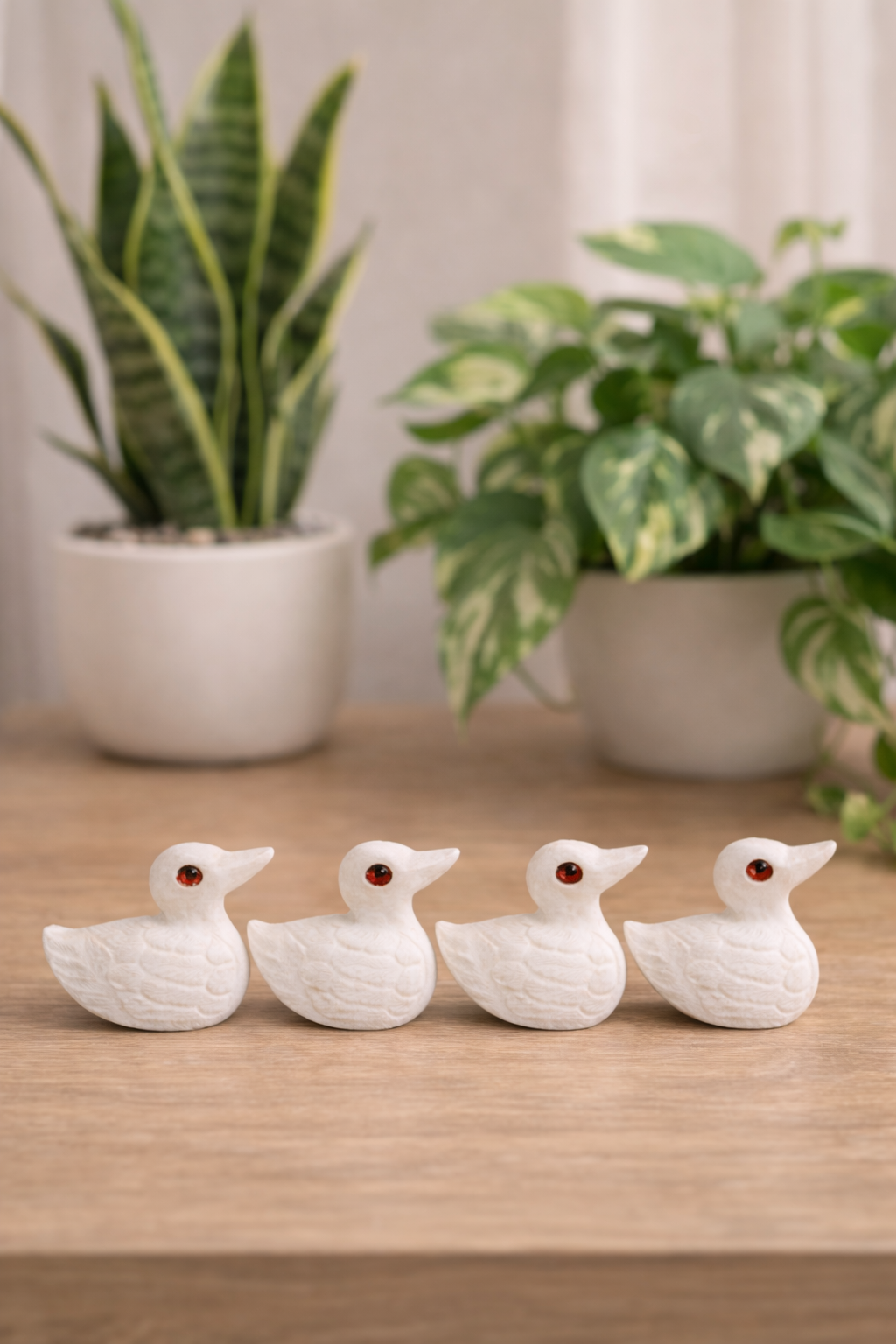 White marble duck figurines with red stone eyes on wooden surface with potted indoor plants