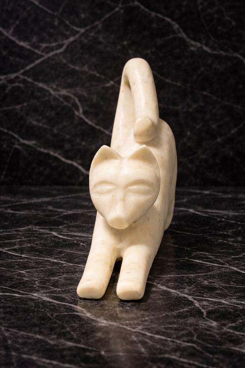 Polished white marble cat statue in stretching pose on dark marble table, luxury home décor NZ