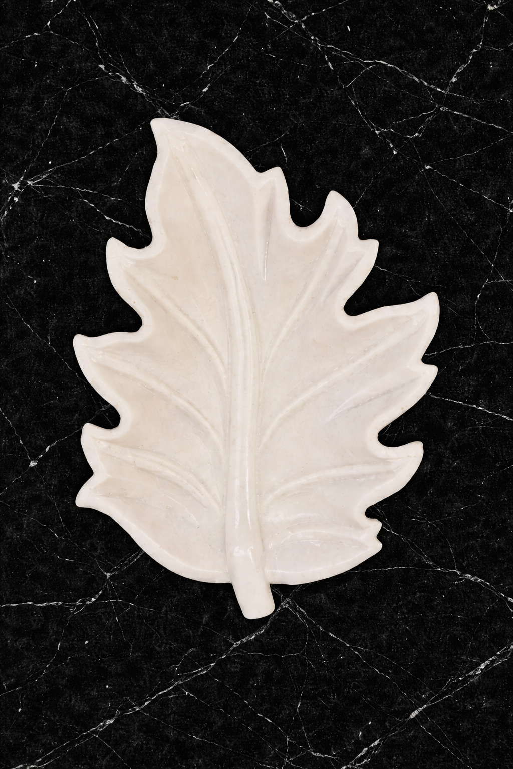 Marble leaf bowl NZ in polished white stone on a black marble background.