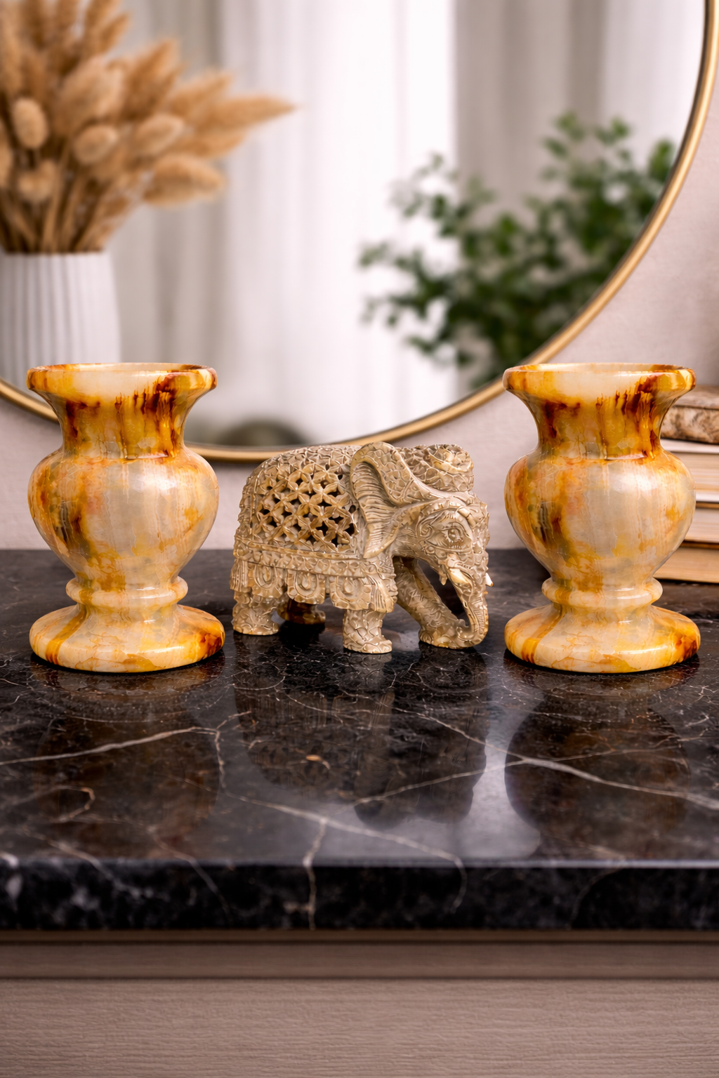 Handcrafted onyx elephant figurine placed between two polished amber onyx pots on a black marble tabletop with mirror background, luxury home decor NZ.