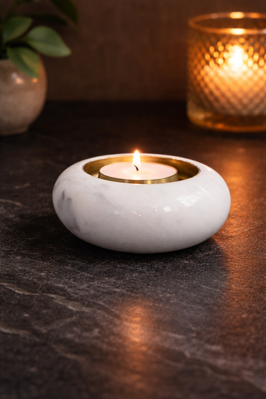 Round white marble tealight holder with brass insert and lit candle on black marble table, luxury home décor NZ