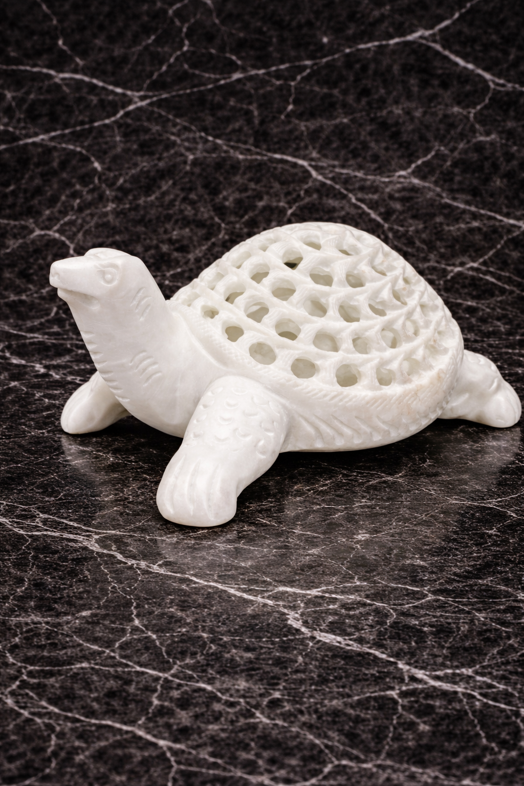 Hand-carved white marble turtle sculpture with lattice shell design on black marble background
