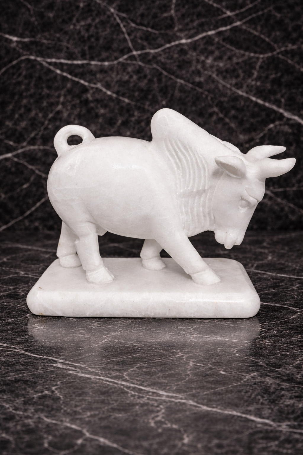 Hand-carved white marble bull sculpture standing on marble base against black marble background