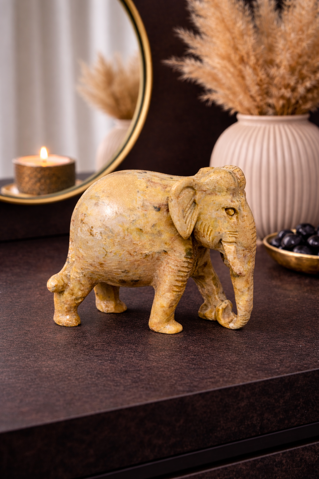 Hand-carved polished stone elephant figurine decor placed on a dark table with candle and vase in a living room setting.