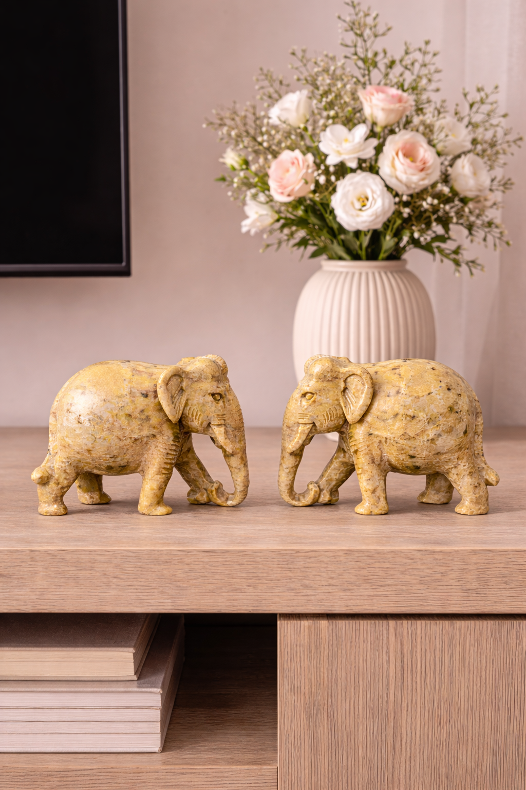 Pair of hand-carved polished stone elephant figurines placed on a wooden table with vase of flowers in living room decor.