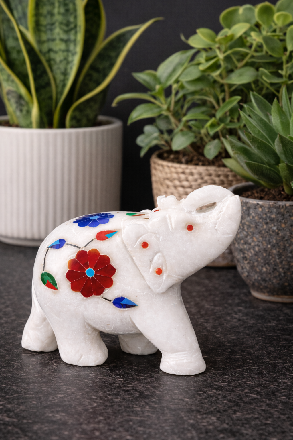 Decorative white marble elephant sculpture with colourful stone inlay displayed with indoor plants