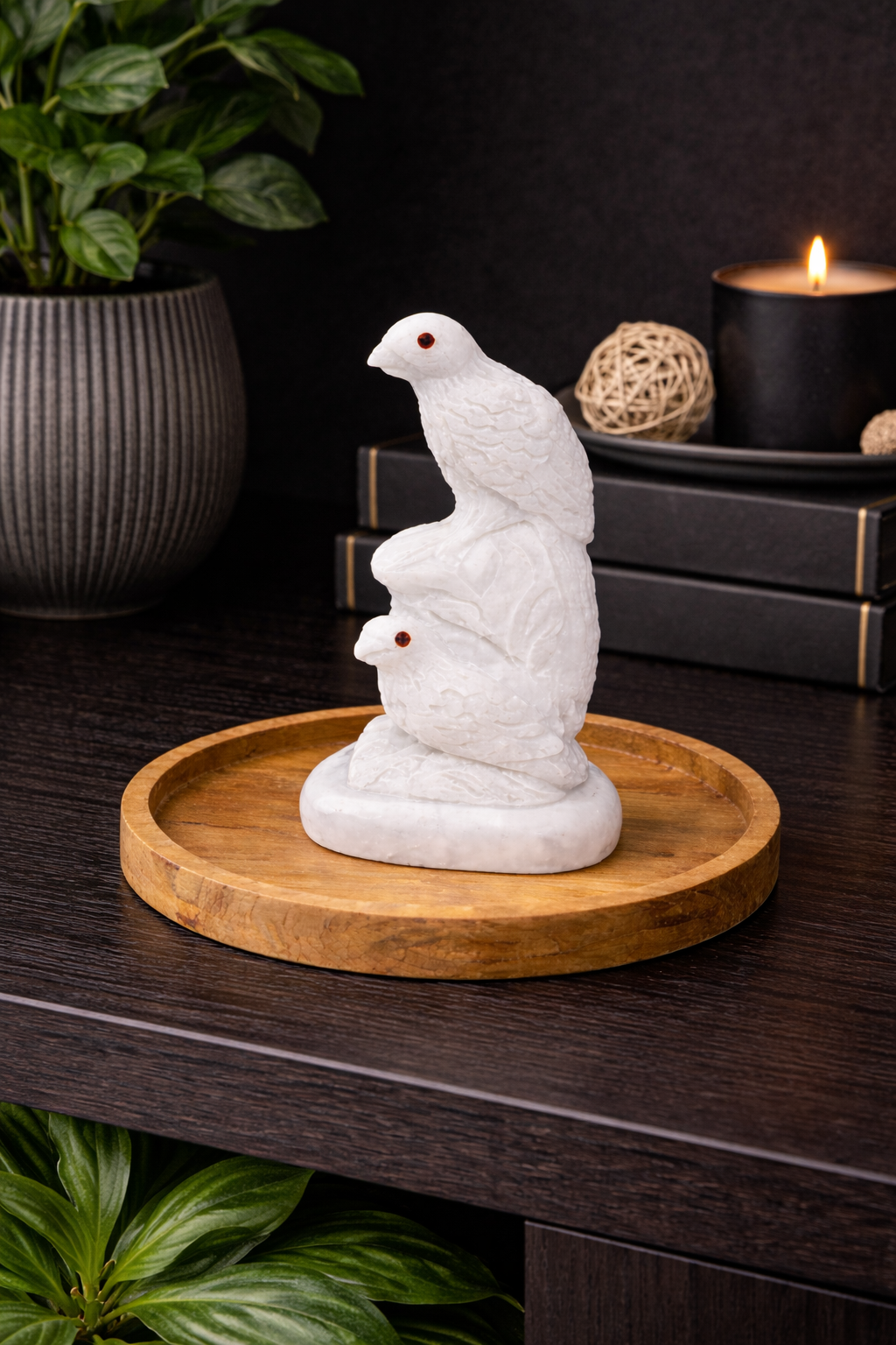 White marble bird figurine pair displayed on round wooden tray with candle and plant styling