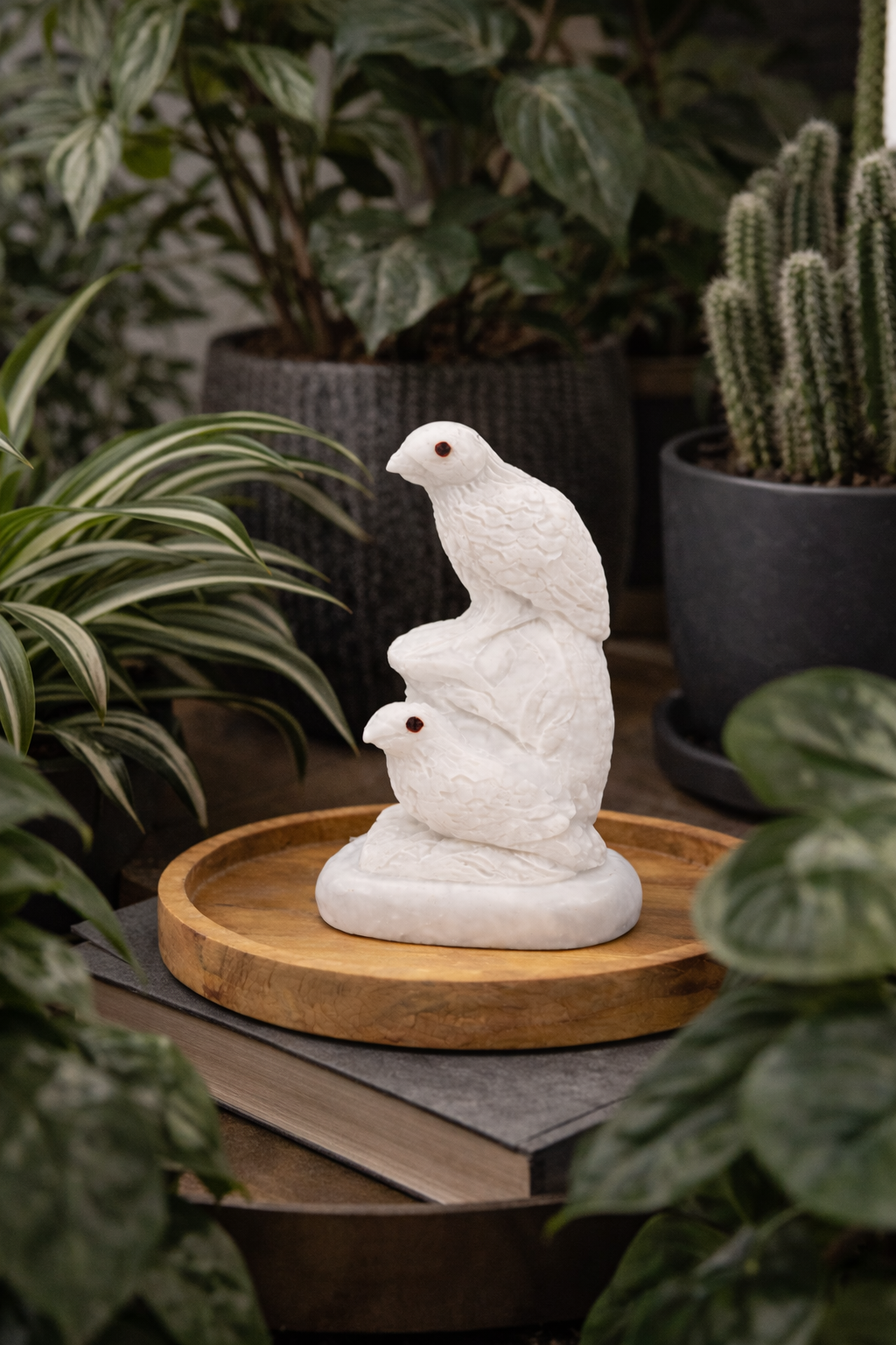 Hand-carved white marble bird sculpture displayed on wooden tray with indoor plants