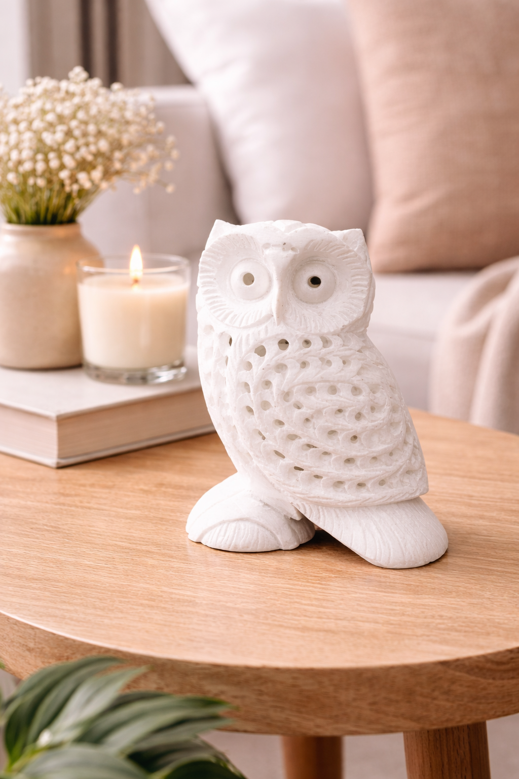 White marble owl figurine with detailed carved feathers displayed on round wooden tray with candle and neutral décor styling