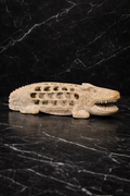 Hand-carved soapstone crocodile figurine with intricate hollow carving displayed on black marble surface