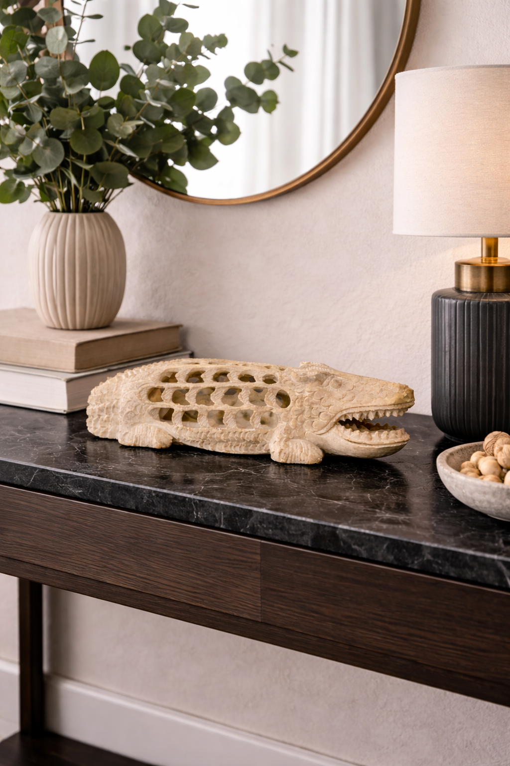 Hand-carved soapstone crocodile figurine styled on dark marble console table with lamp and indoor plant in modern home interior