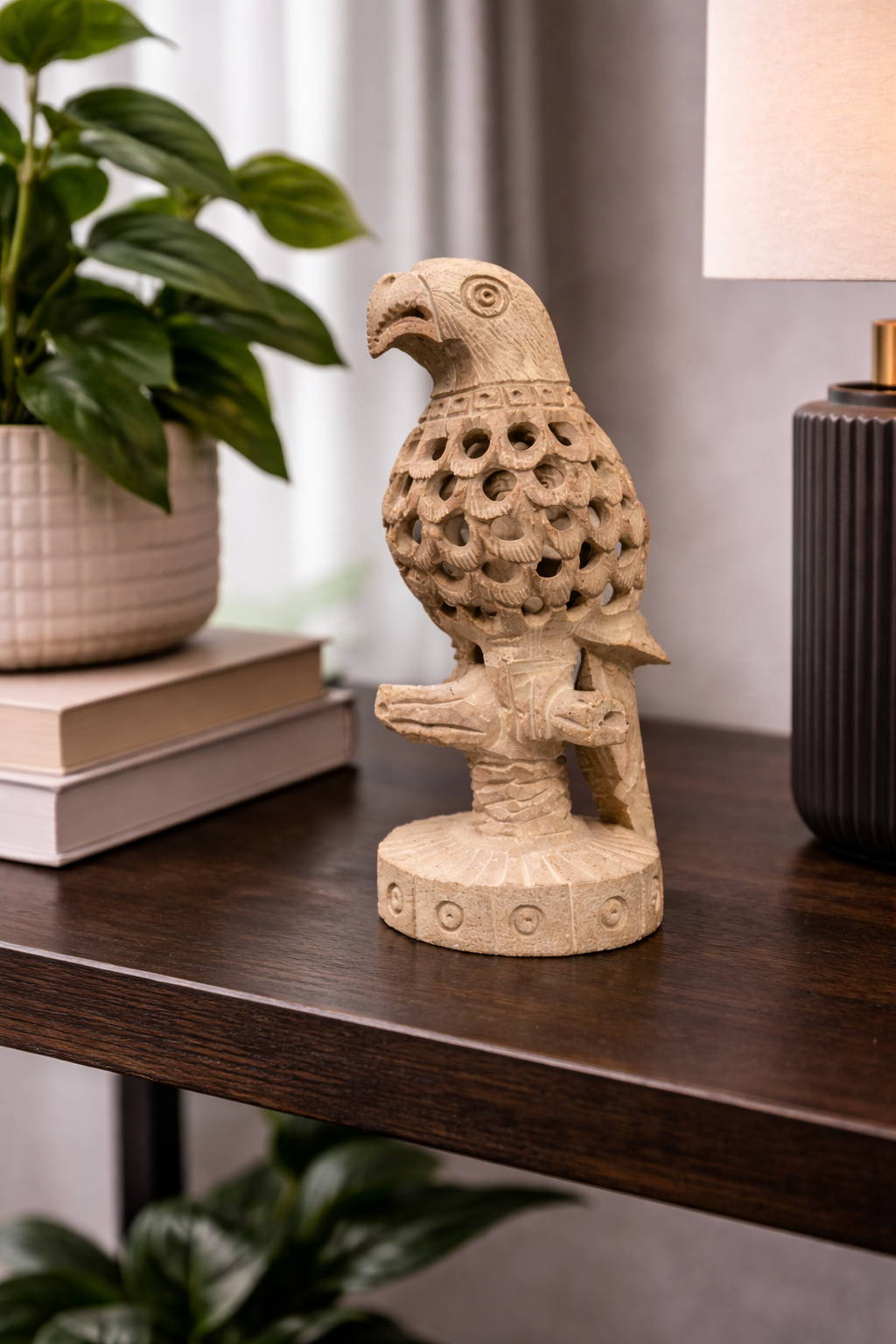Hand-carved soapstone parrot sculpture displayed on wooden console table with lamp and indoor plant in modern home interior