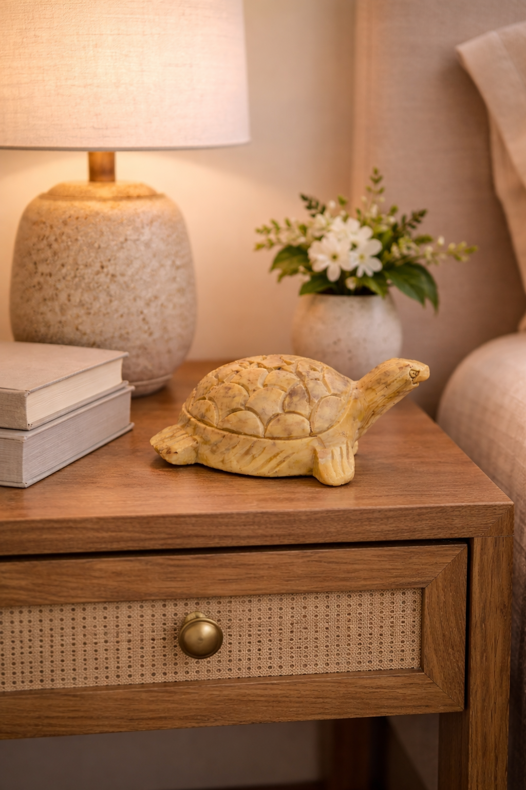 Polished soapstone turtle sculpture styled on wooden nightstand with lamp and flowers