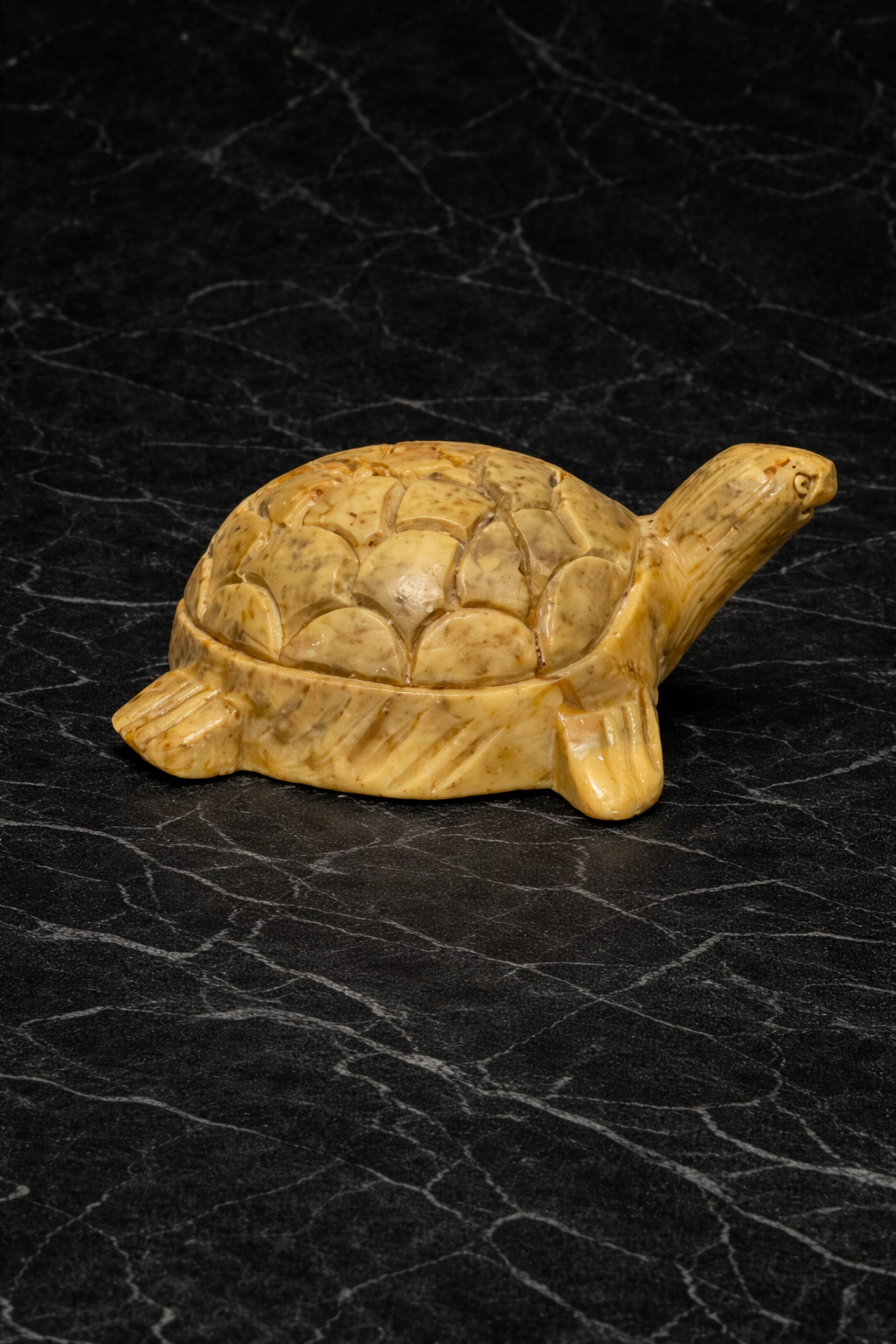 Polished soapstone turtle sculpture with carved shell detail on black marble surface