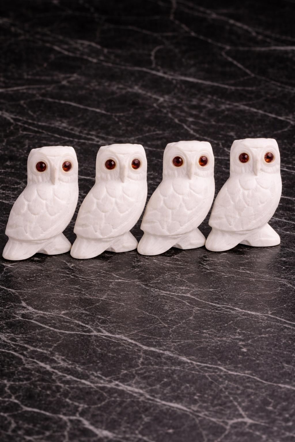 Four white marble owl figurines with red stone eyes displayed on dark marble surface in NZ home décor